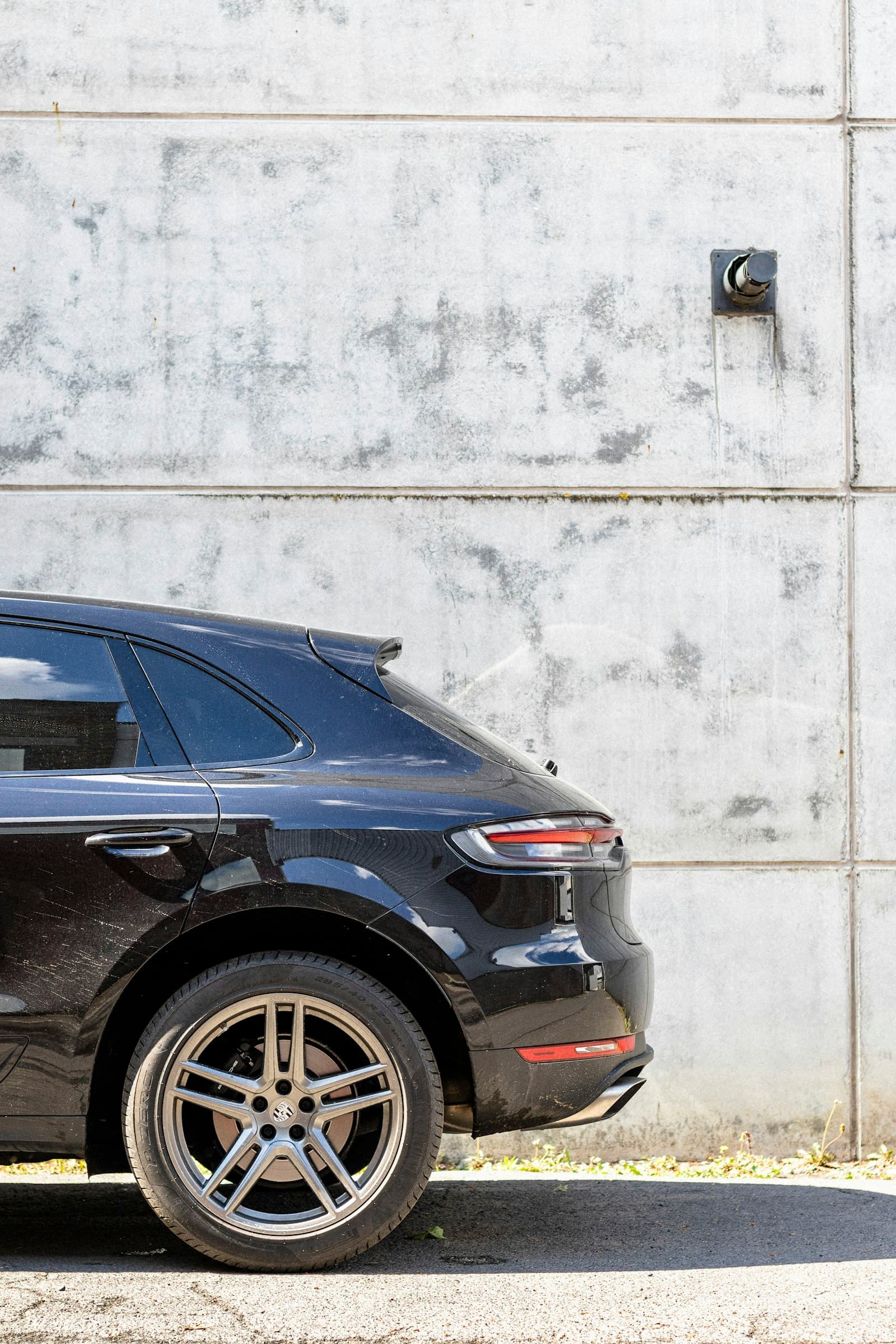 Rear quarter of a black Porsche Macan beside a concrete wall