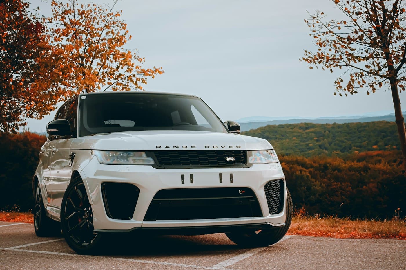 White Range Rover Sport parked beside autumn trees